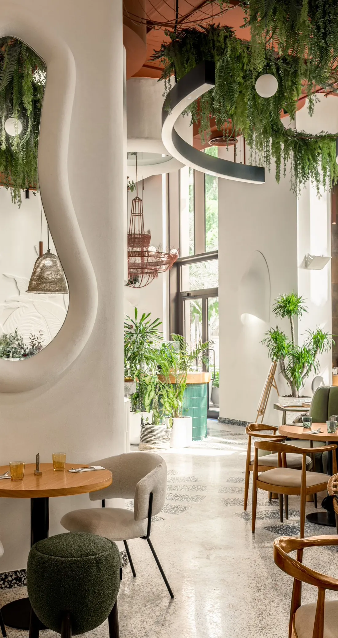 A sculpted white column with an S-shaped mirror niche, hanging ferns and a green pouf at Café de Palma