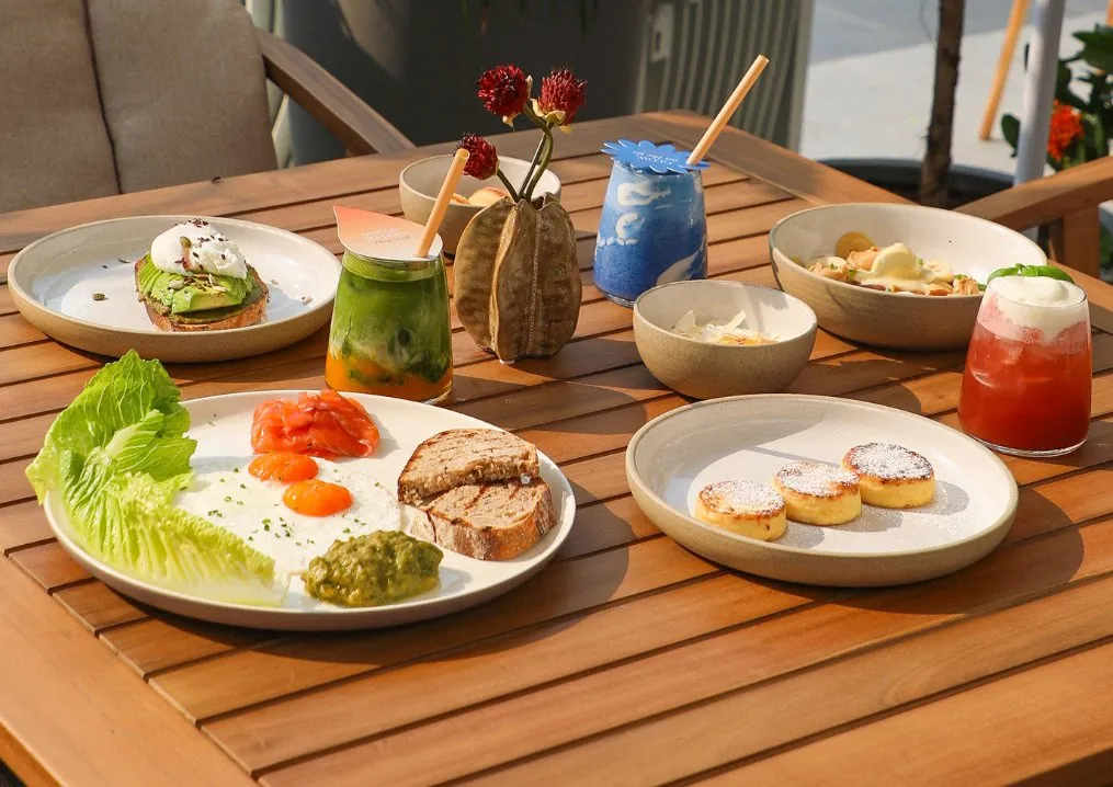 A breakfast table with eggs, avocado toast, ricotta syrniki and smoothies in the sun