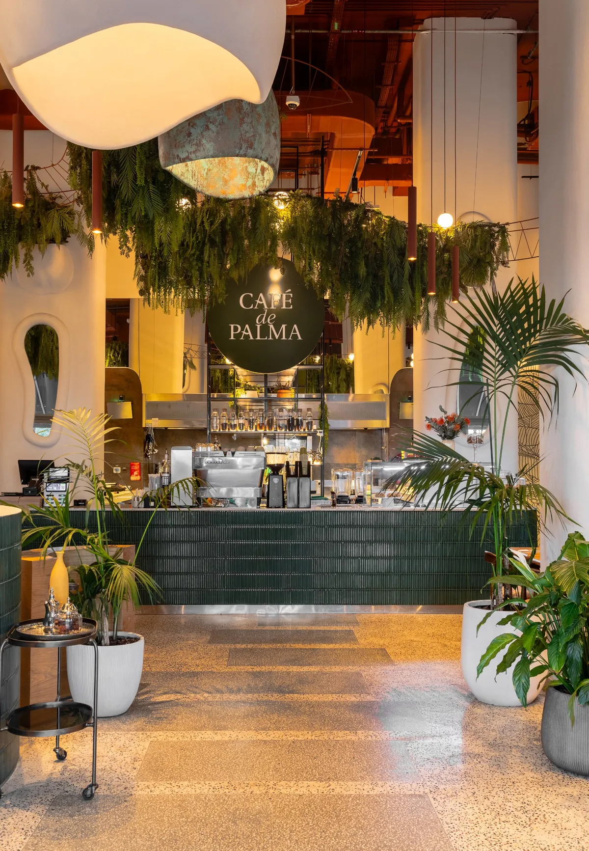 The coffee bar at Café de Palma Creek Harbour under the round sign, with palms and hanging greenery