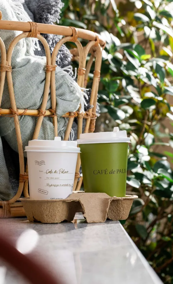 An olive and a white Café de Palma cup by a rattan chair