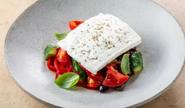 Greek salad with a slab of feta over tomato, cucumber and olives