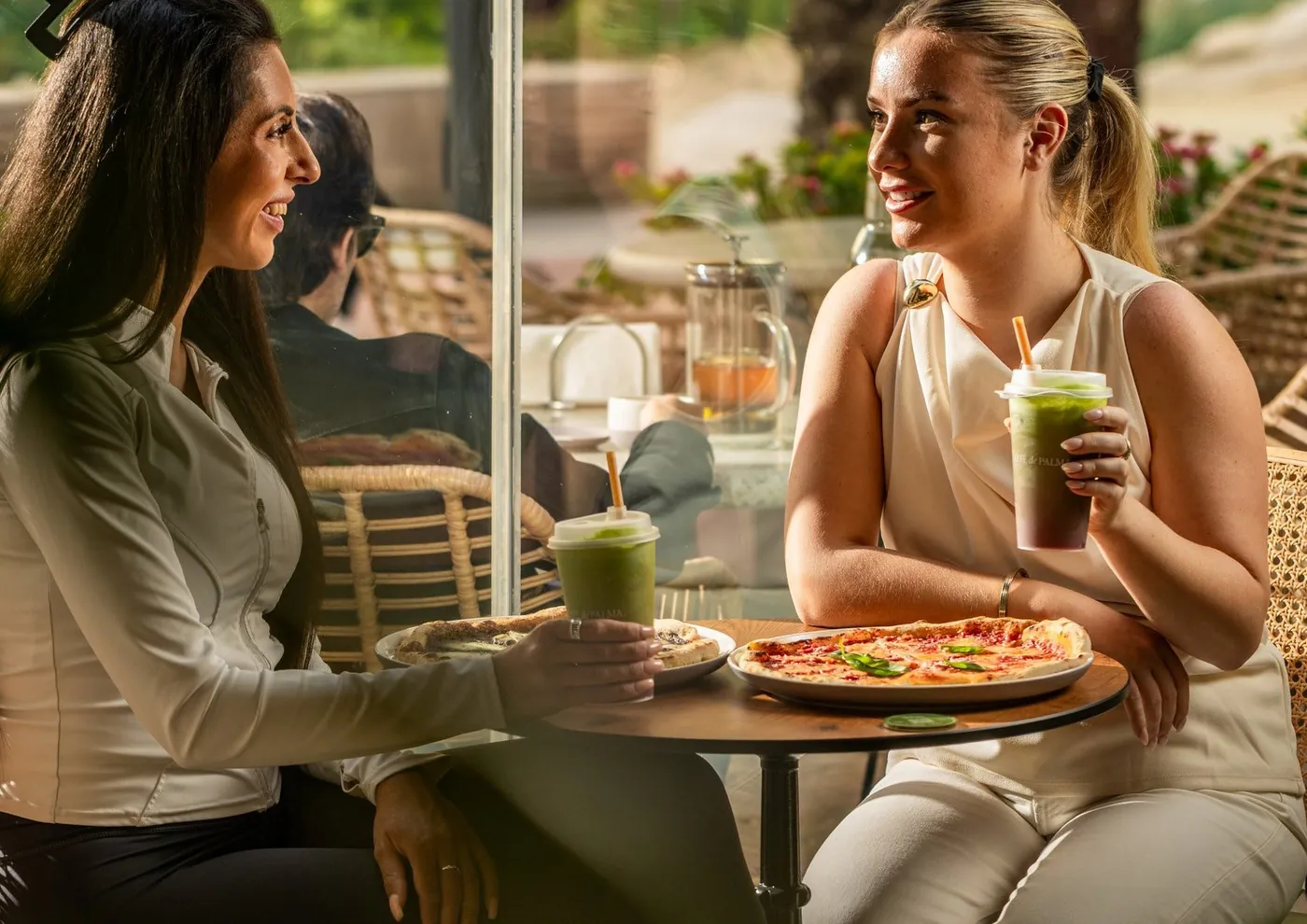 Two friends sharing a pizza and green smoothies at a terrace table